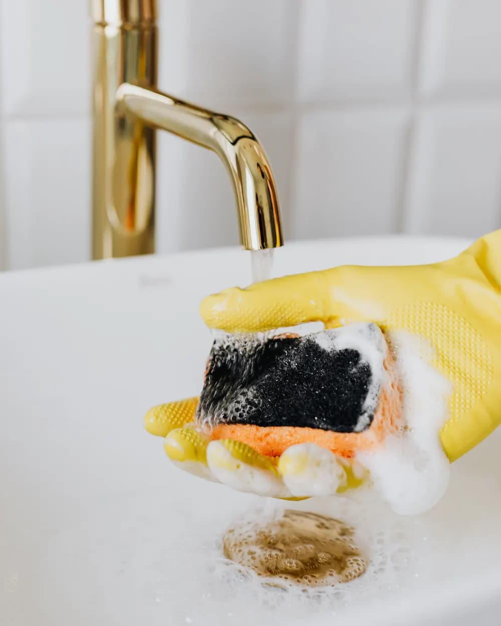 Gloved hands with a foaming sponge cleaning at a kitchen sink